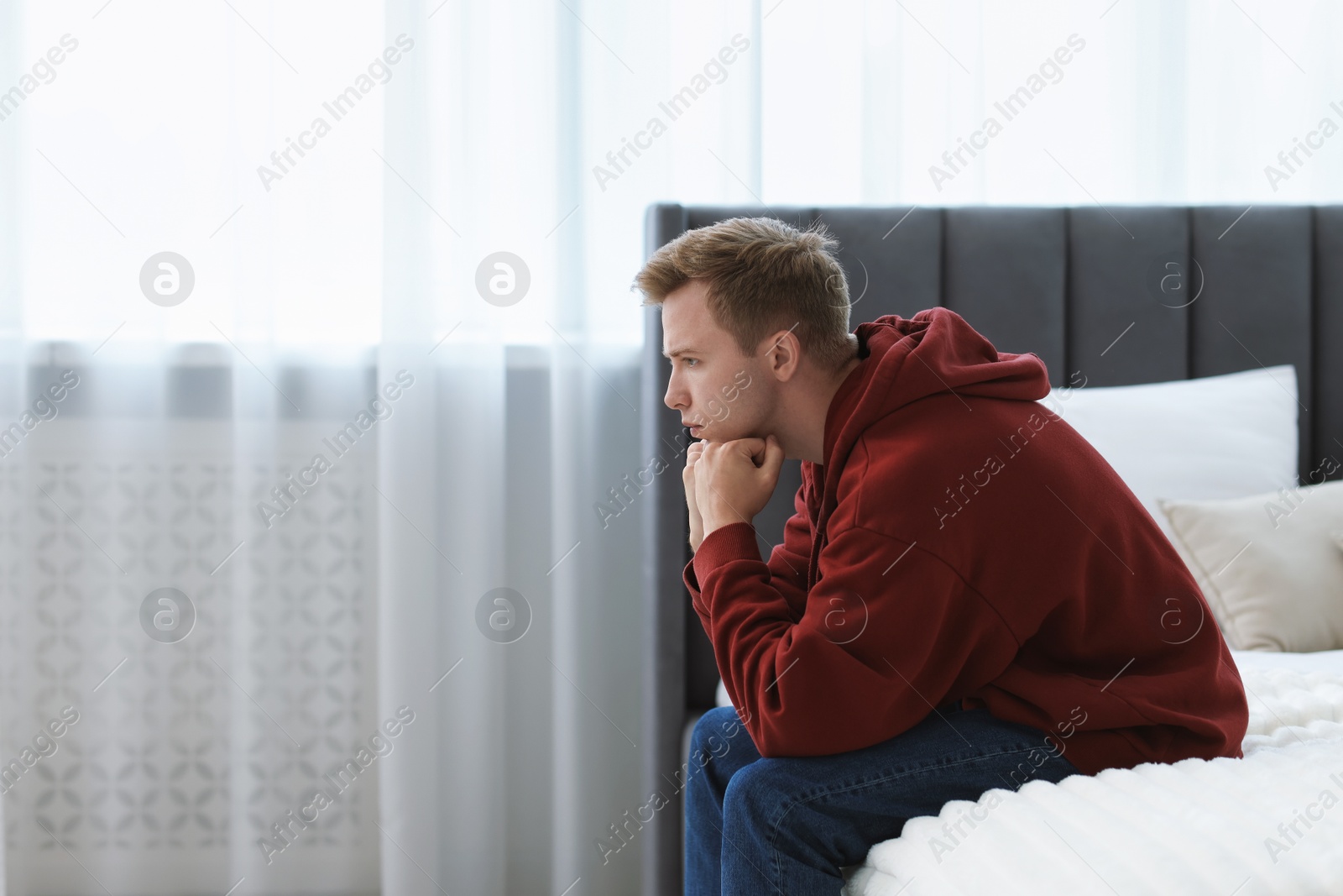 Sad thoughtful man sitting on bed at home. Space for text Photo of Sad thoughtful man sitting on bed at home. Space for text