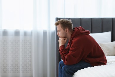 Photo of Sad thoughtful man sitting on bed at home. Space for text