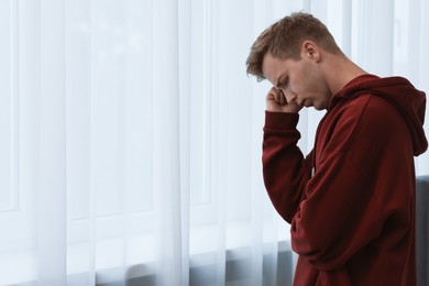 Photo of Sad thoughtful man near window at home. Space for text