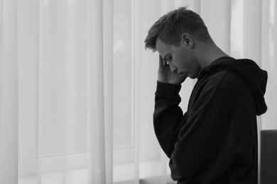 Photo of Sad thoughtful man near window at home, space for text. Black and white effect