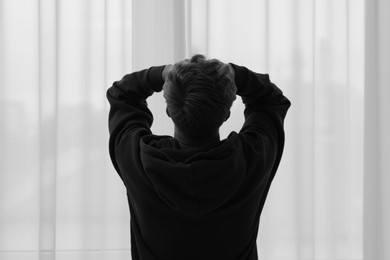 Photo of Silhouette of sad man near window at home, back view. Black and white effect