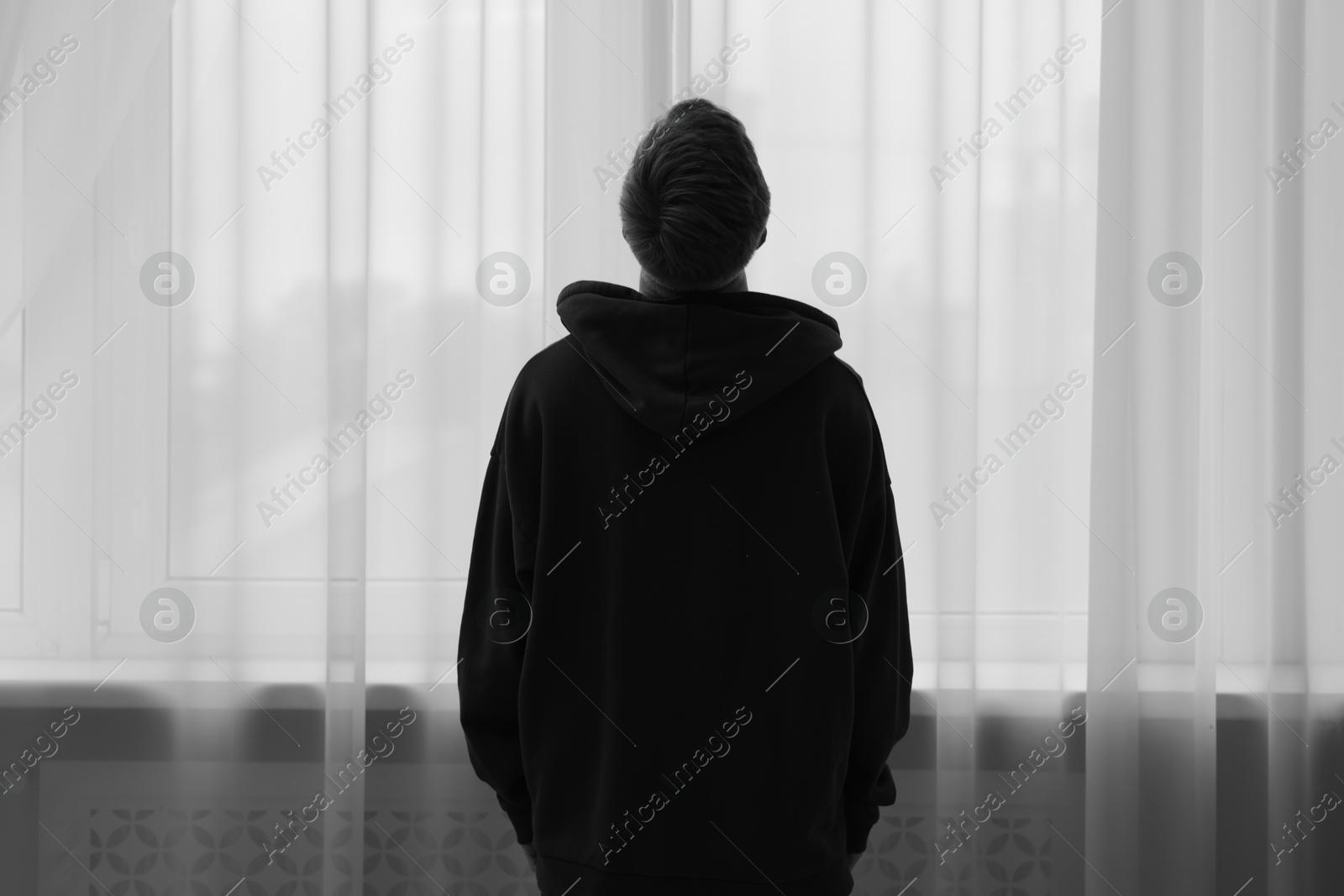 Silhouette of sad man near window at home, back view. Black and white effect Photo of Silhouette of sad man near window at home, back view. Black and white effect