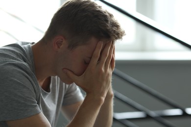 Photo of Sad tired man covering face with hands near railings indoors. Depression