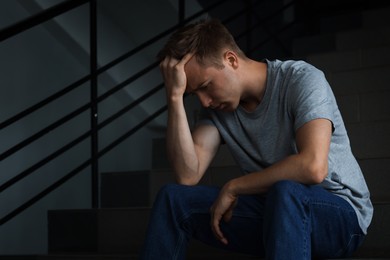 Photo of Sad man sitting on stairs in darkness. Depression