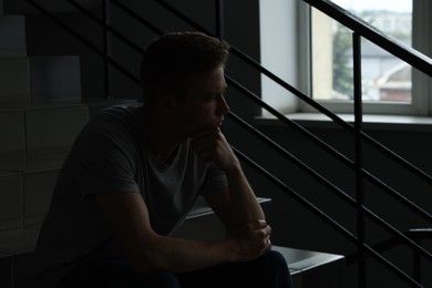 Photo of Sad thoughtful man sitting on stairs in darkness. Depression