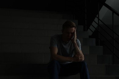 Photo of Sad man sitting on stairs in darkness. Depression