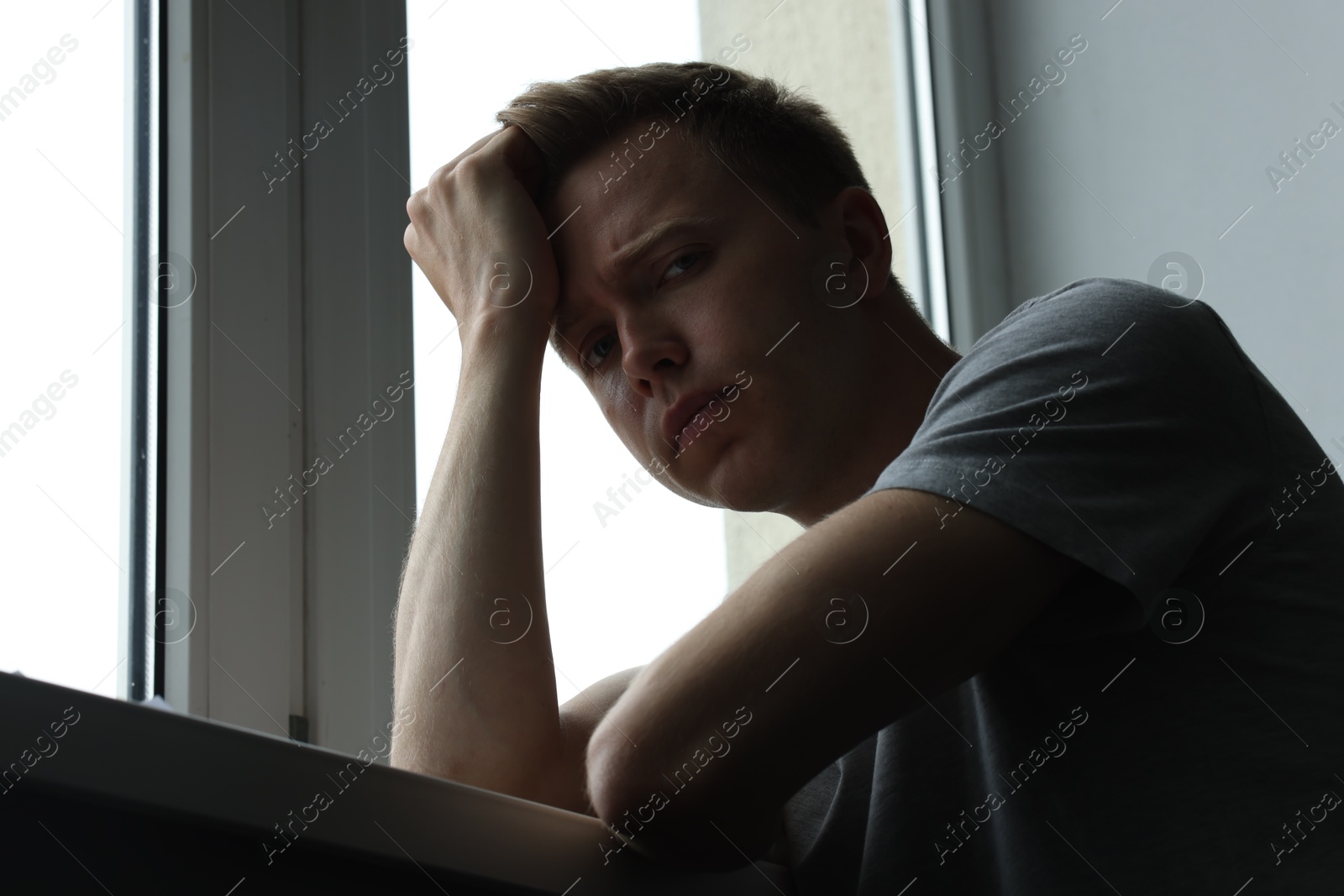 Sad thoughtful man near window indoors, low angle view. Depression Photo of Sad thoughtful man near window indoors, low angle view. Depression