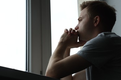 Photo of Sad thoughtful man looking at window indoors, low angle view with space for text. Depression