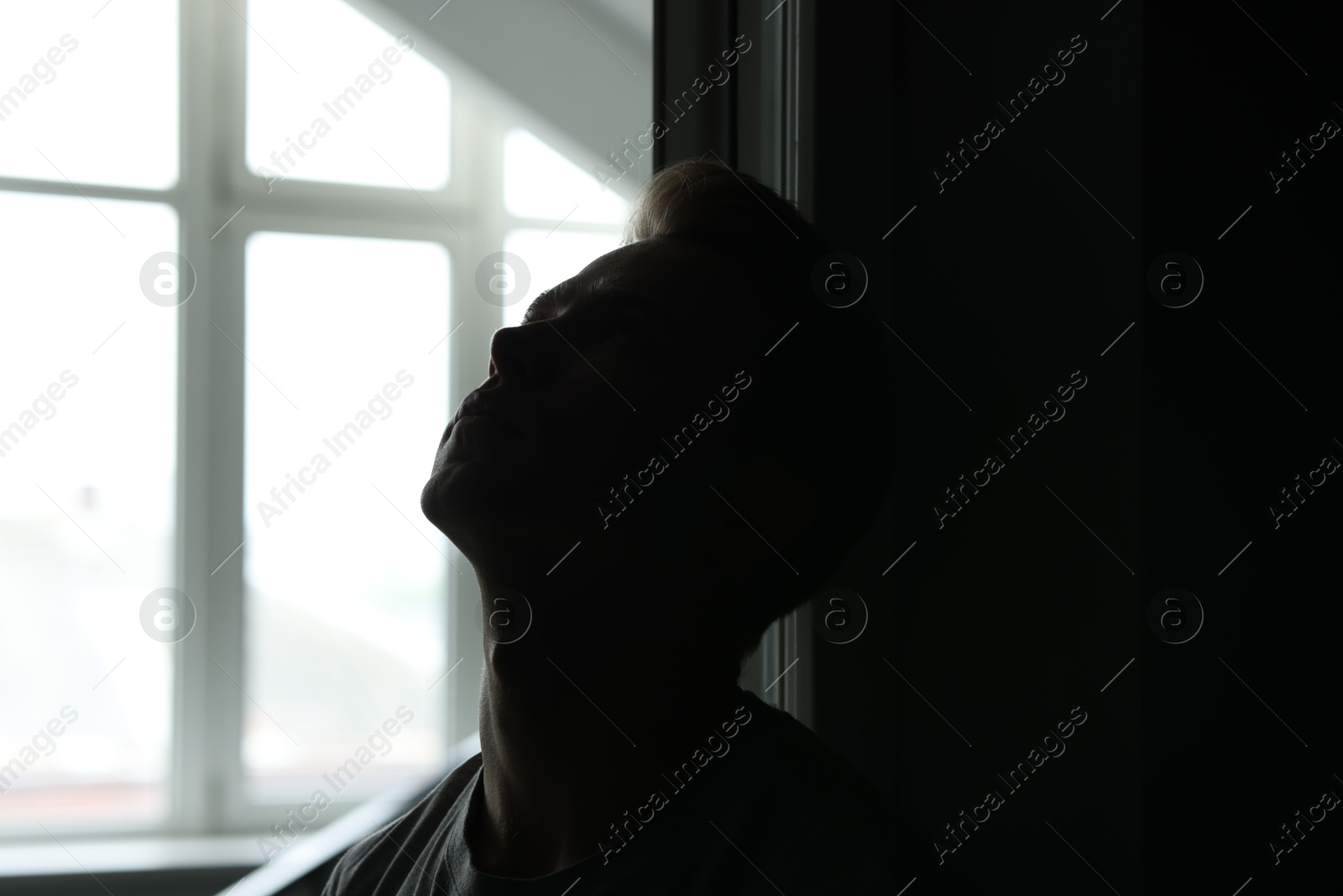 Sadness and depression. Tired man in dark room with open door against window with daylight Photo of Sadness and depression. Tired man in dark room with open door against window with daylight