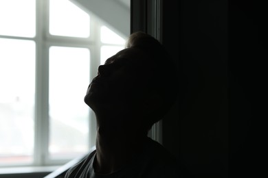 Photo of Sadness and depression. Tired man in dark room with open door against window with daylight
