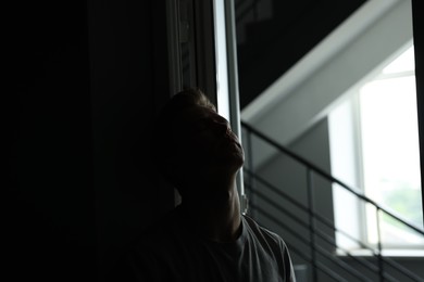 Photo of Sadness and depression. Tired man in dark room with open door and window with daylight