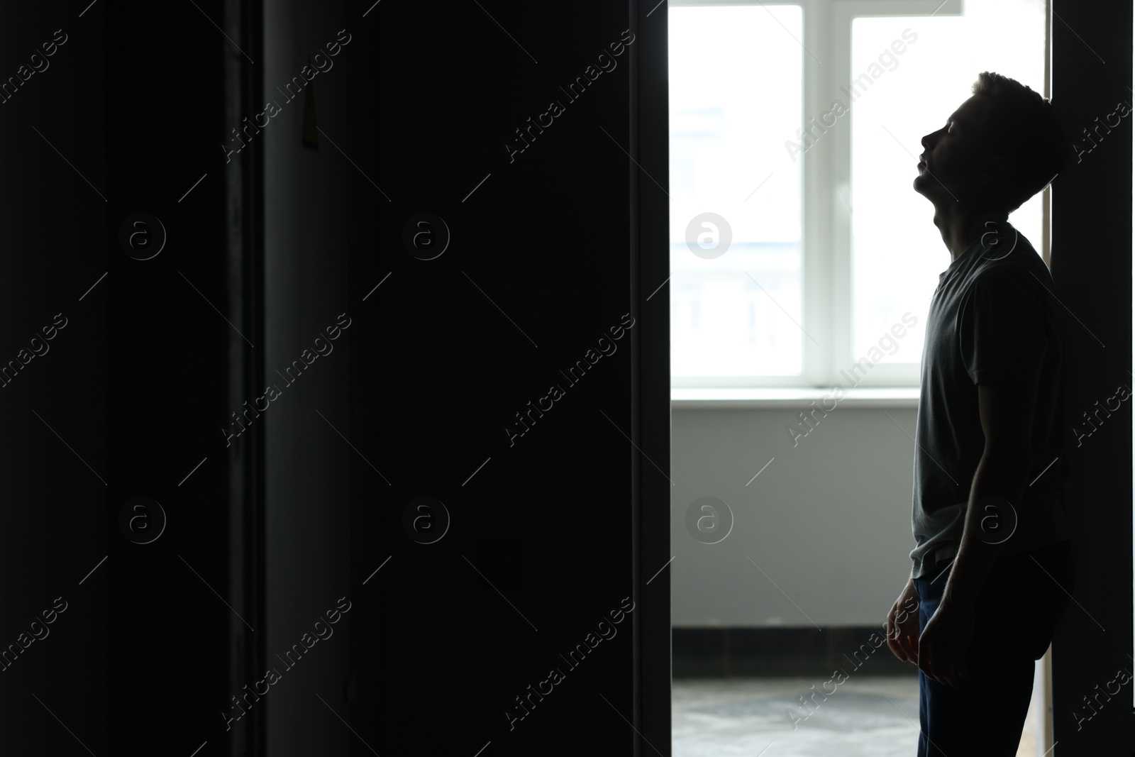Sadness and depression. Tired man in dark room with open door against window with daylight. Space for text Photo of Sadness and depression. Tired man in dark room with open door against window with daylight. Space for text