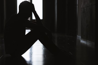 Photo of Sadness and depression. Silhouette of man sitting on floor in dark room
