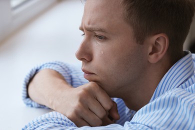Photo of Sad man crying alone indoors, closeup. Depression and anxiety