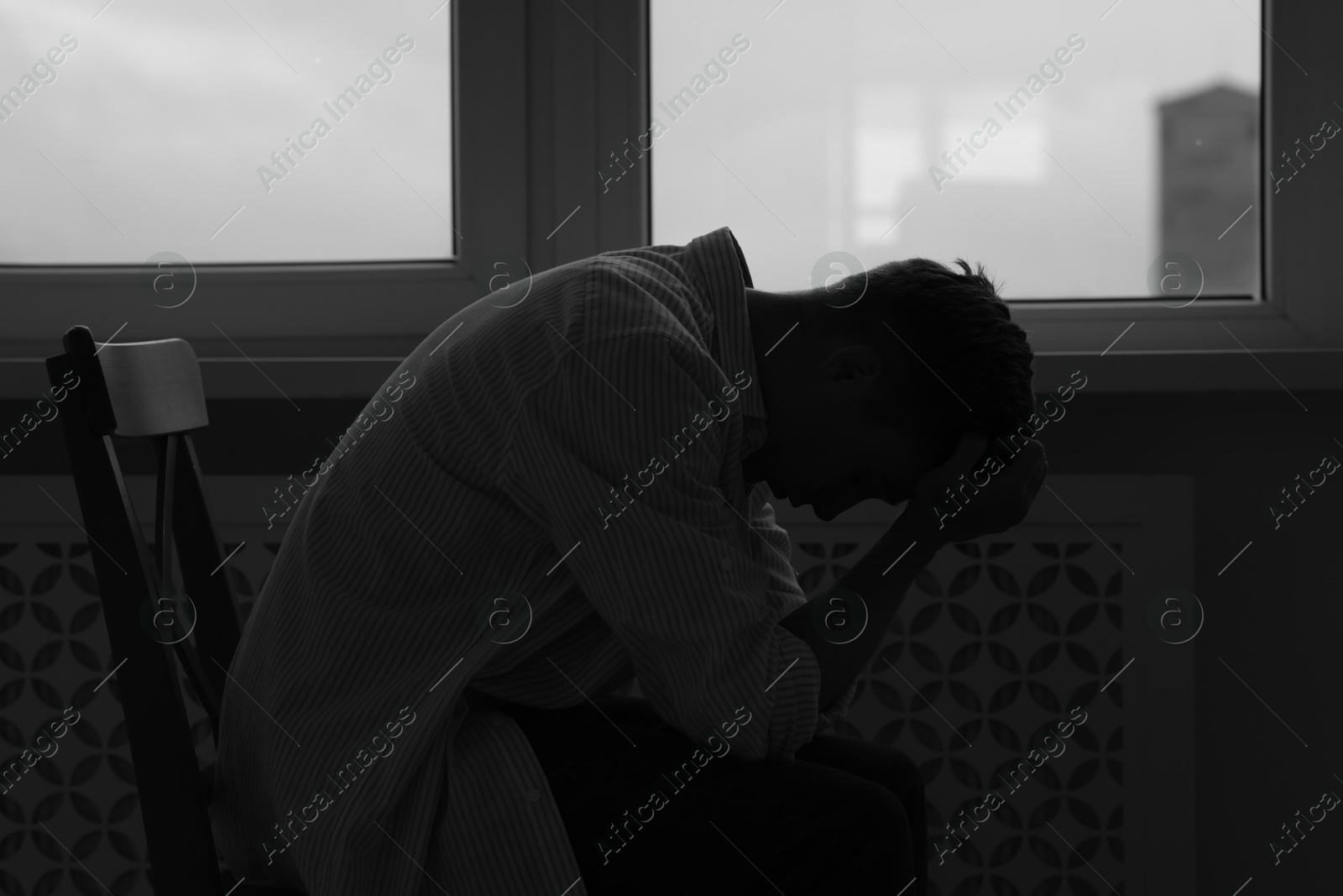 Sad man sitting on chair near window at home. Black and white effect Photo of Sad man sitting on chair near window at home. Black and white effect
