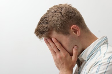 Photo of Sad tired man covering face with hand on light background. Space for text