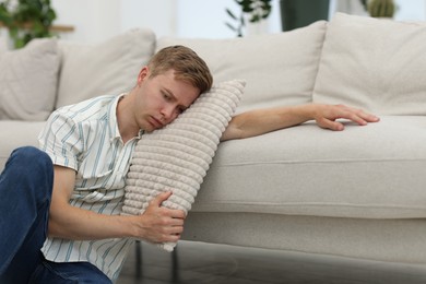 Photo of Sad tired man with pillow leaning on sofa at home