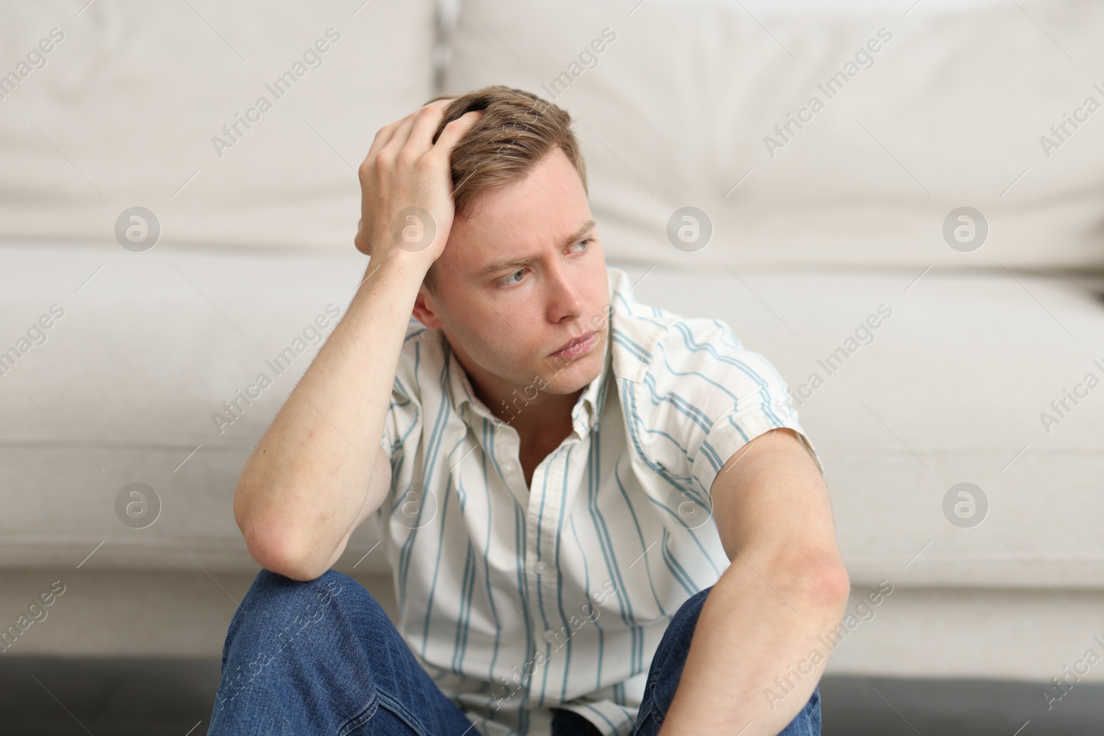 Sad thoughtful man sitting near sofa at home Photo of Sad thoughtful man sitting near sofa at home
