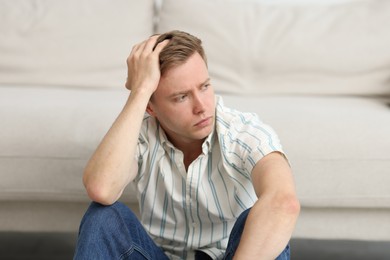 Photo of Sad thoughtful man sitting near sofa at home