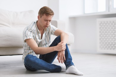 Photo of Sad thoughtful man sitting on floor at home