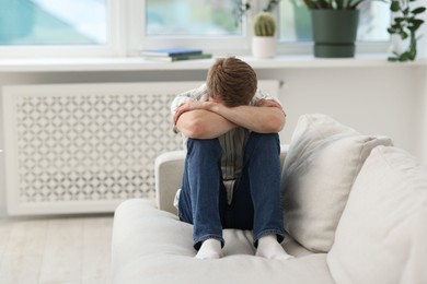 Photo of Sad man sitting on sofa at home, space for text