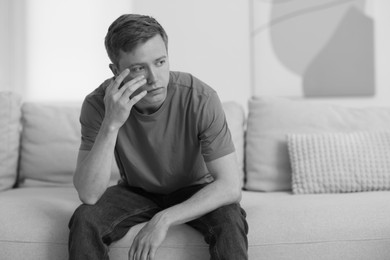 Photo of Sad thoughtful man on sofa at home. Black and white effect