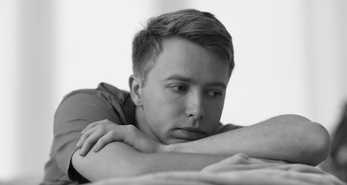 Photo of Sad thoughtful man on blurred grey background, black and white effect