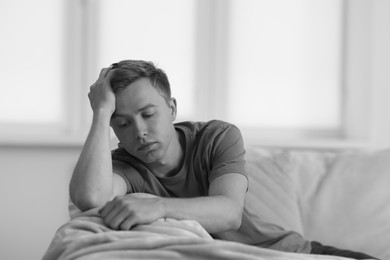 Photo of Sad thoughtful man on sofa at home, black and white effect