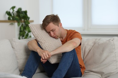 Photo of Sad man with pillow sitting on sofa at home