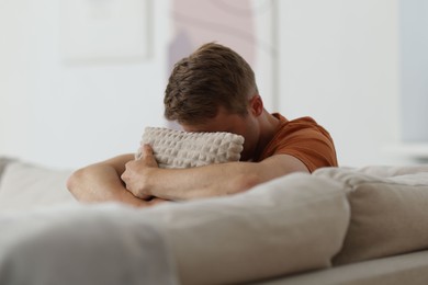 Photo of Sad man hugging pillow on sofa at home