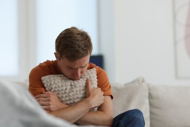 Photo of Sad man hugging pillow on sofa at home