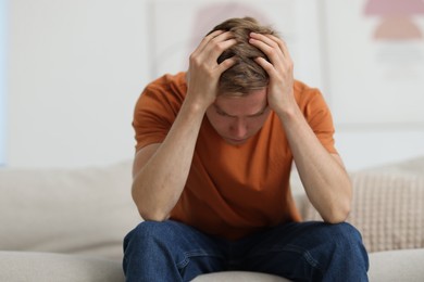 Photo of Sad man sitting on sofa at home