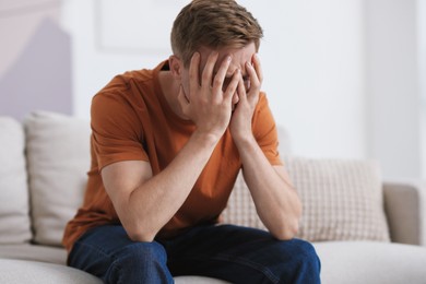 Photo of Sad man covering face with hands on sofa at home