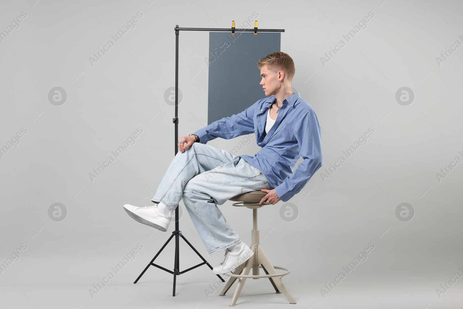 Photo of Handsome young man wearing stylish clothes sitting on chair against light grey background