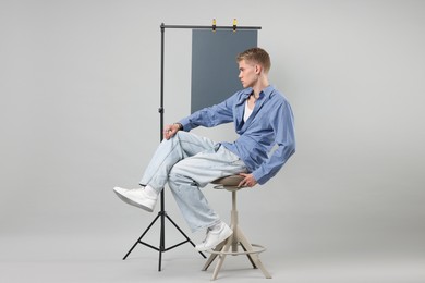 Photo of Handsome young man wearing stylish clothes sitting on chair against light grey background