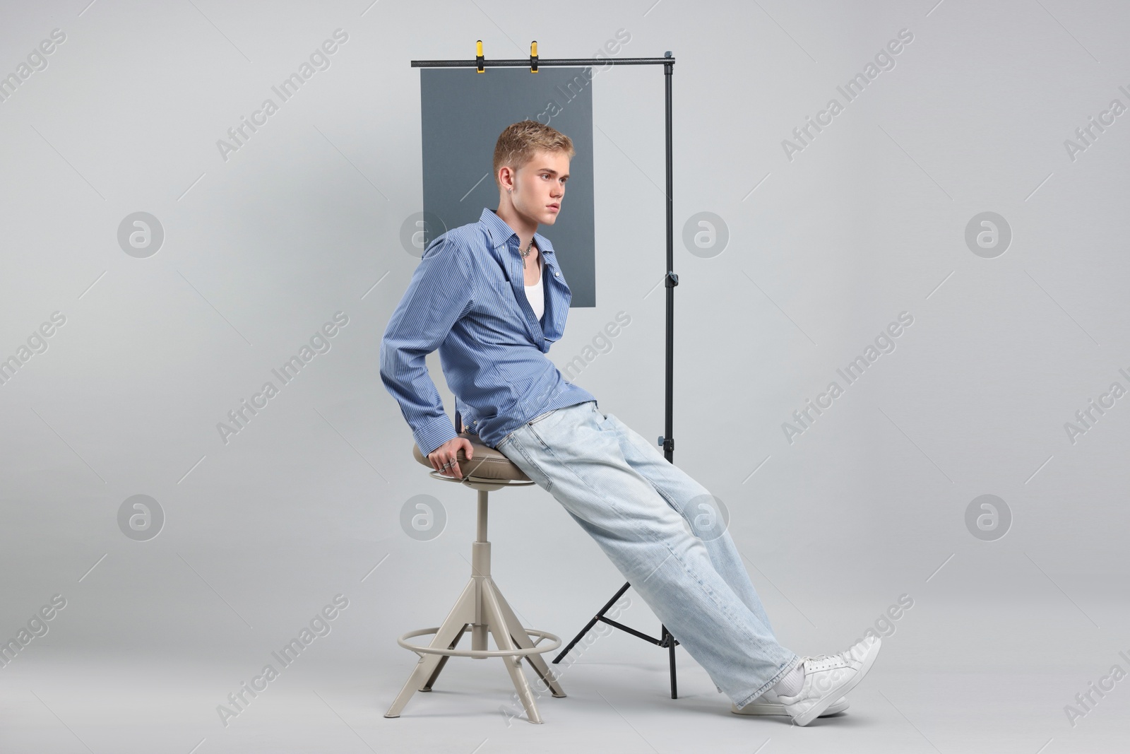 Photo of Handsome young man wearing stylish clothes sitting on chair against light grey background