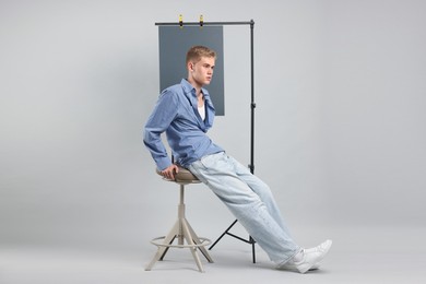 Photo of Handsome young man wearing stylish clothes sitting on chair against light grey background