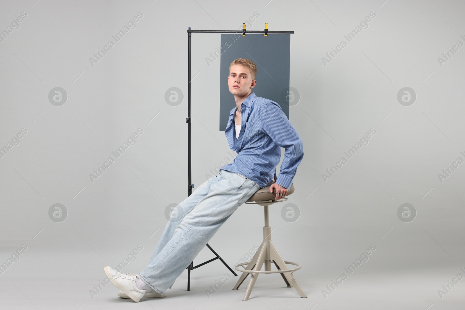 Photo of Handsome young man wearing stylish clothes sitting on chair against light grey background