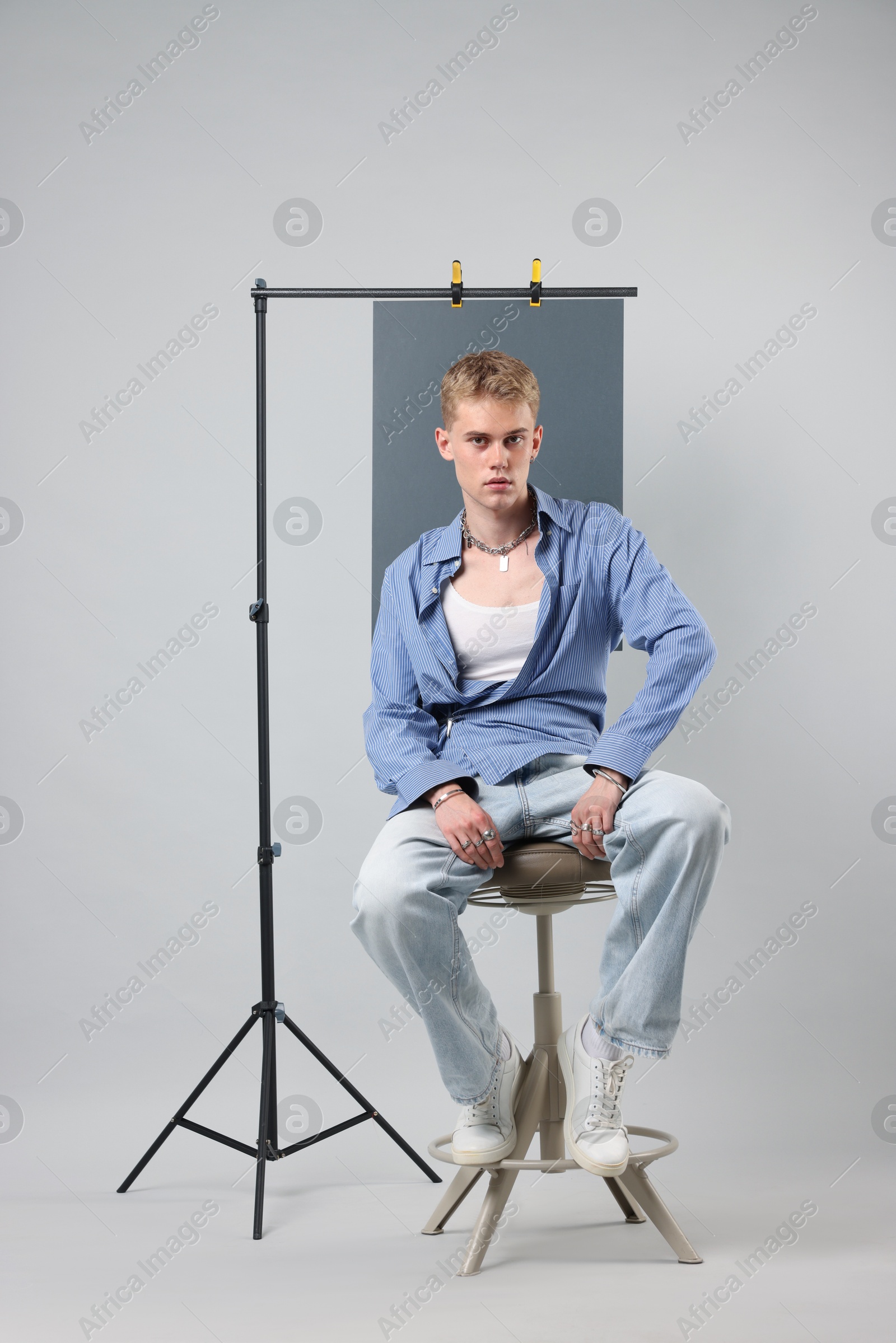 Photo of Handsome young man wearing stylish clothes sitting on chair against light grey background