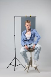 Photo of Handsome young man wearing stylish clothes sitting on chair against light grey background
