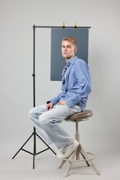 Photo of Handsome young man wearing stylish clothes sitting on chair against light grey background