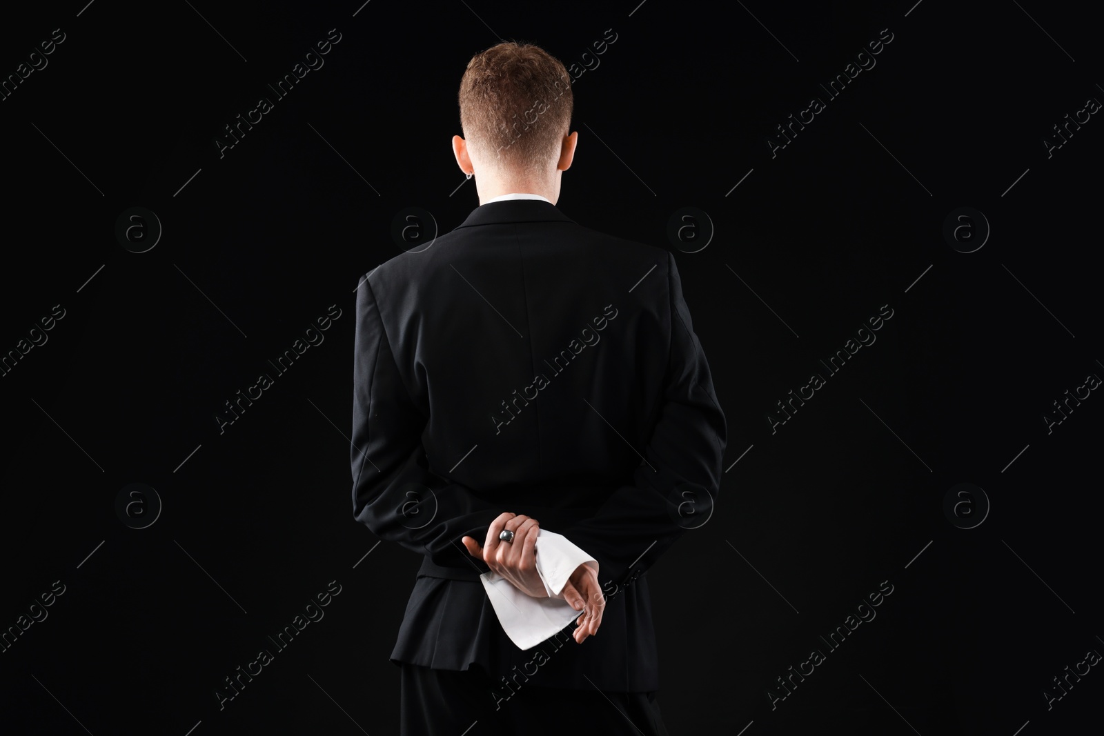 Photo of Young man wearing stylish suit on black background, back view