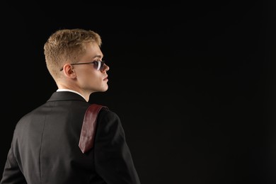 Photo of Handsome young man wearing stylish suit and sunglasses on black background, space for text