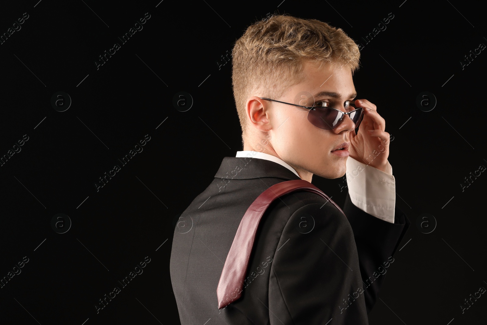 Photo of Handsome young man wearing stylish suit and sunglasses on black background