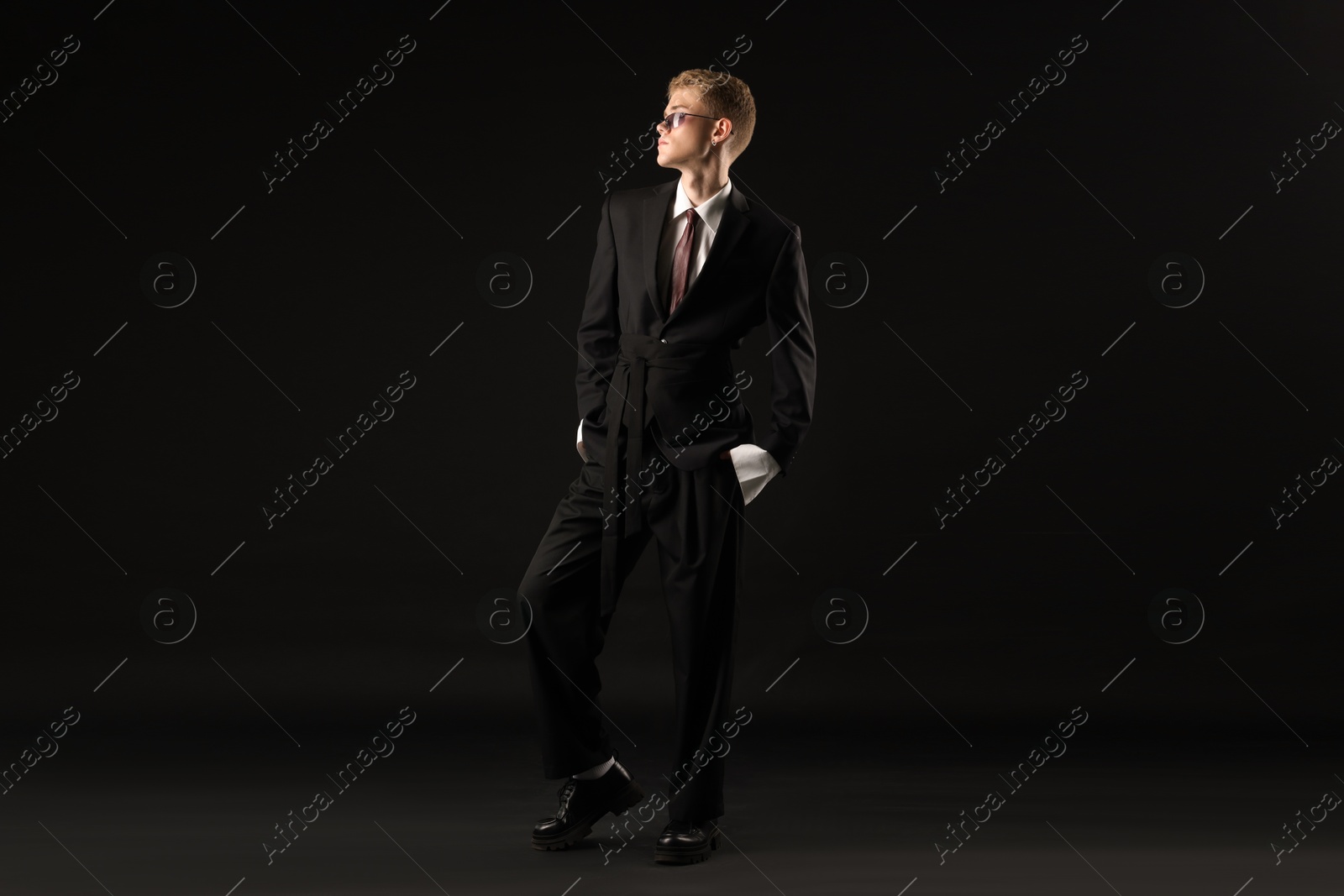Photo of Handsome young man wearing stylish suit and sunglasses on black background