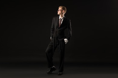 Photo of Handsome young man wearing stylish suit and sunglasses on black background