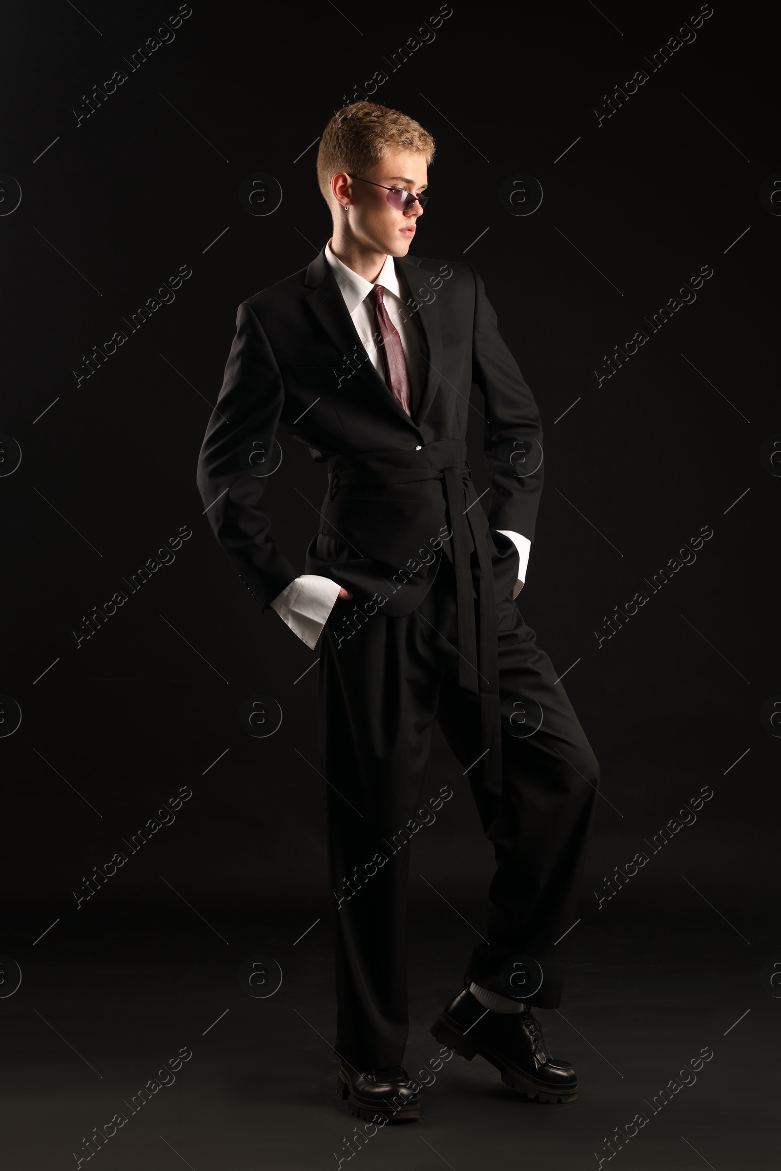 Photo of Handsome young man wearing stylish suit and sunglasses on black background