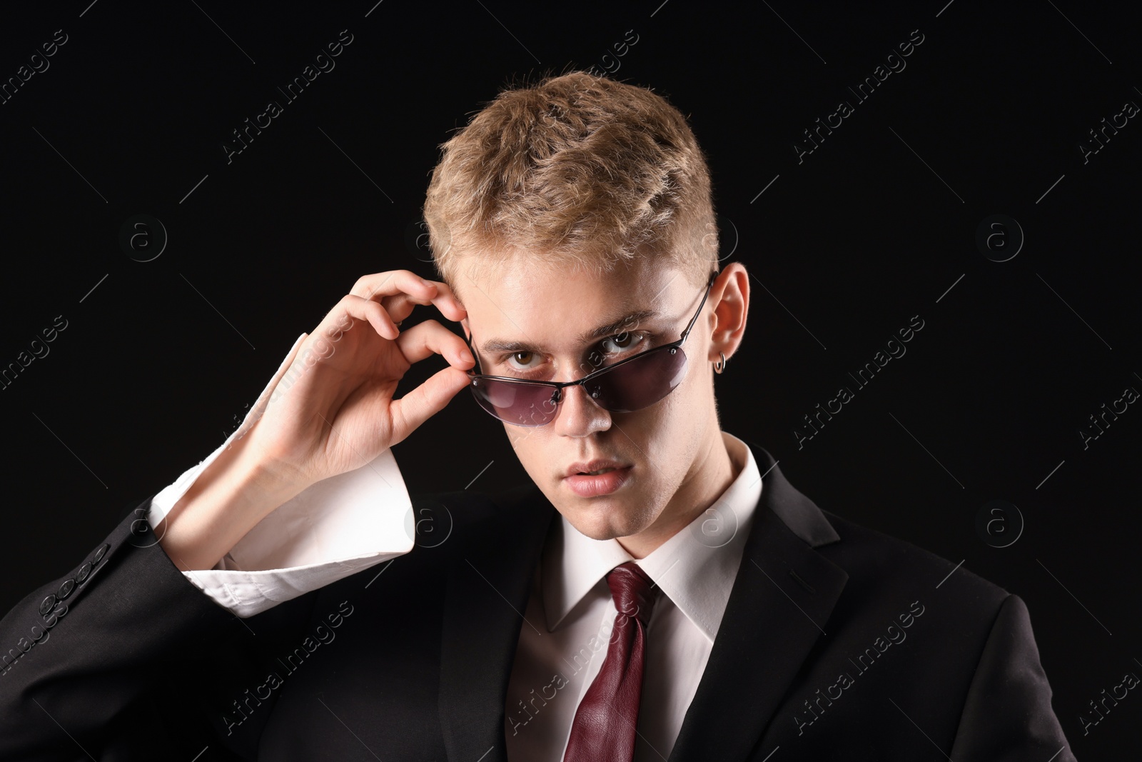 Photo of Handsome young man wearing stylish suit and sunglasses on black background