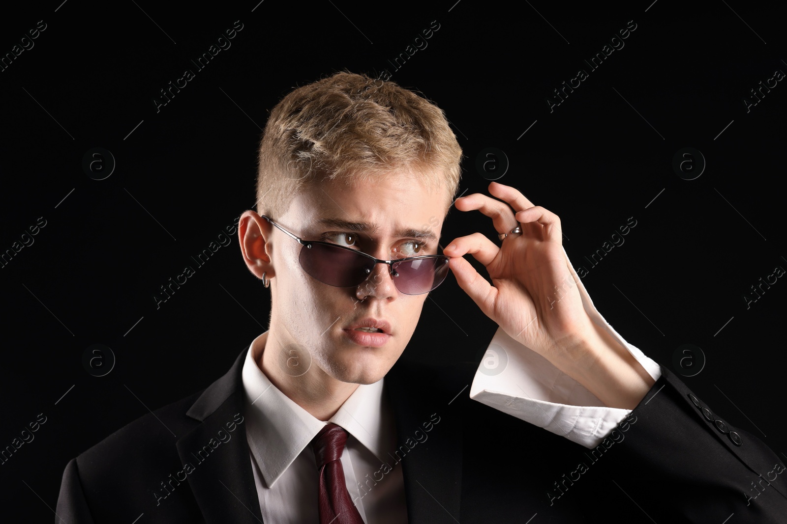 Photo of Handsome young man wearing stylish suit and sunglasses on black background