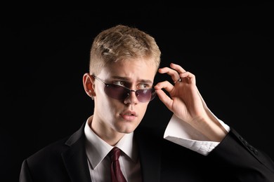 Photo of Handsome young man wearing stylish suit and sunglasses on black background